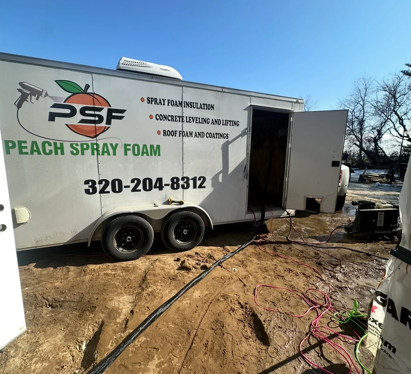 Spray foam insulation trailer with equipment hoses and application gear on job site