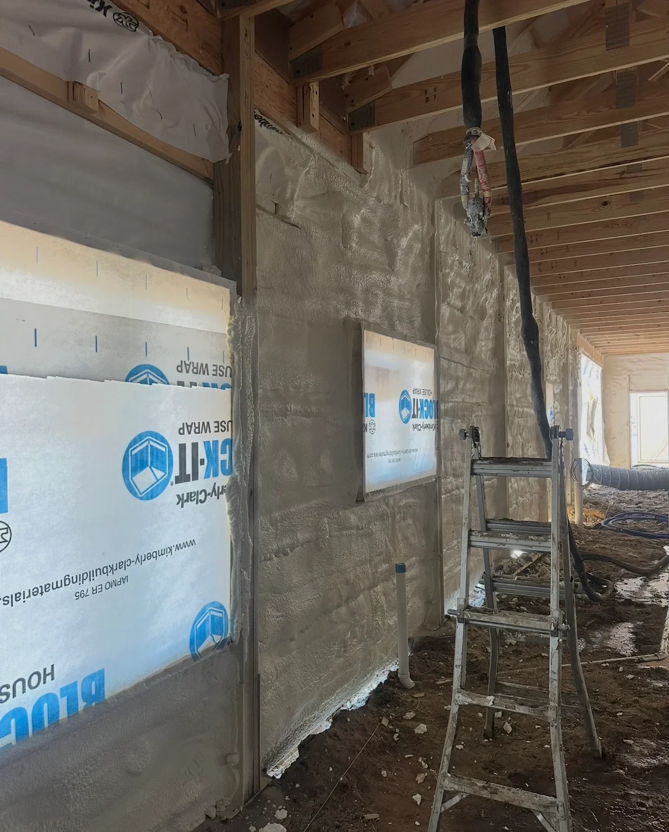 Spray foam insulation applied to interior wall framing with protective sheeting and vapor barriers