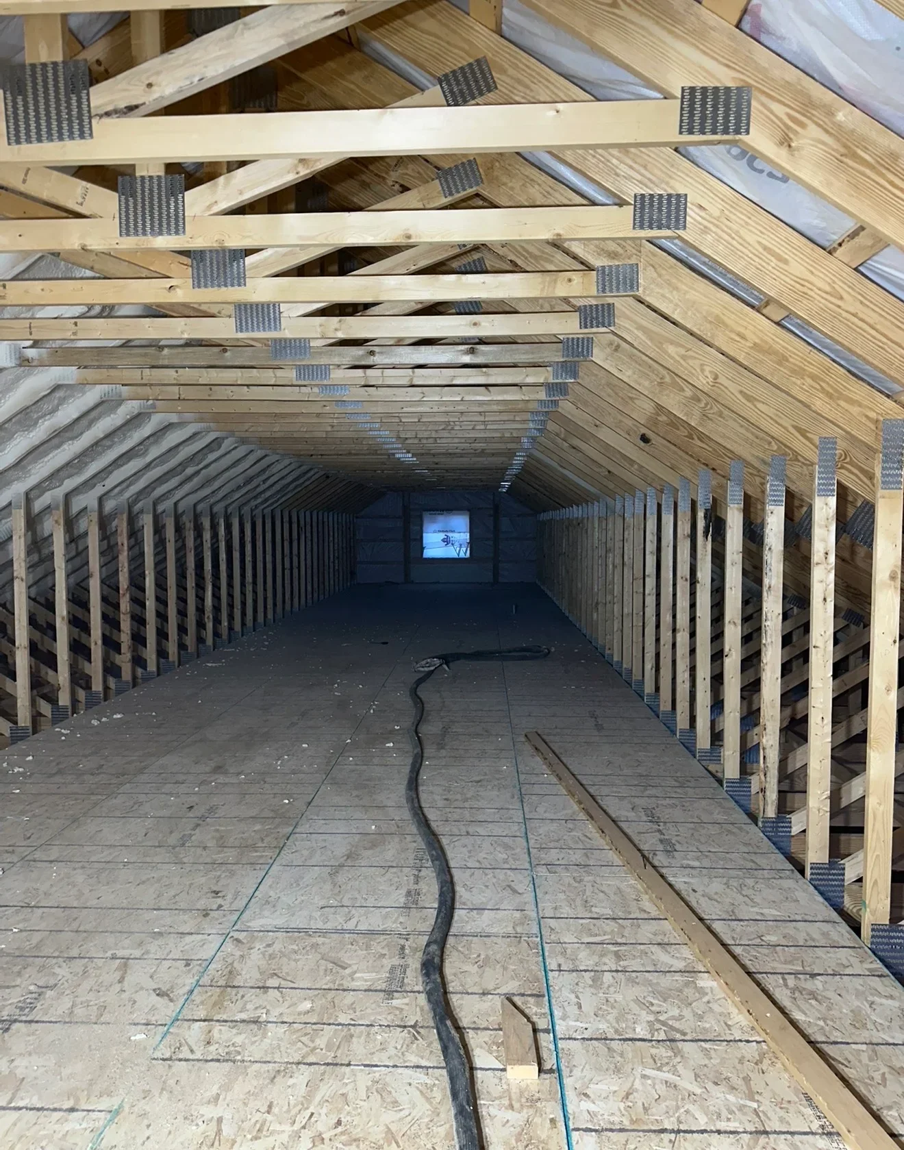 Attic framing with wooden trusses, metal plates, and OSB flooring ready for insulation