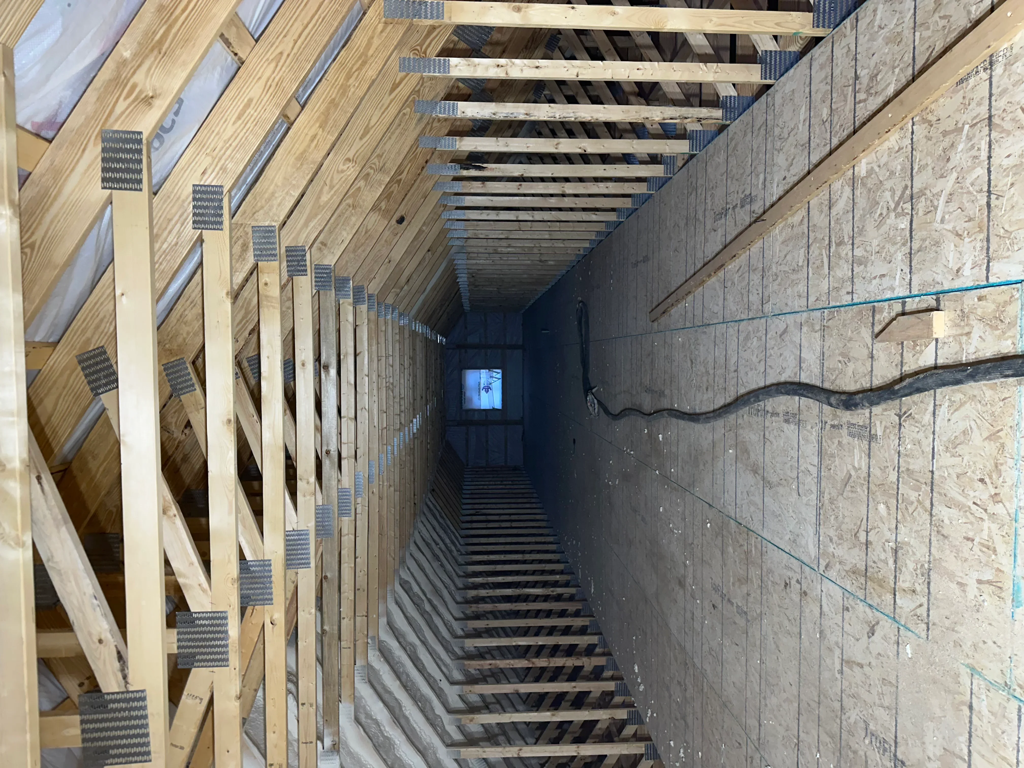 Open joist cavity with spray foam insulation between wooden beams and metal bridging