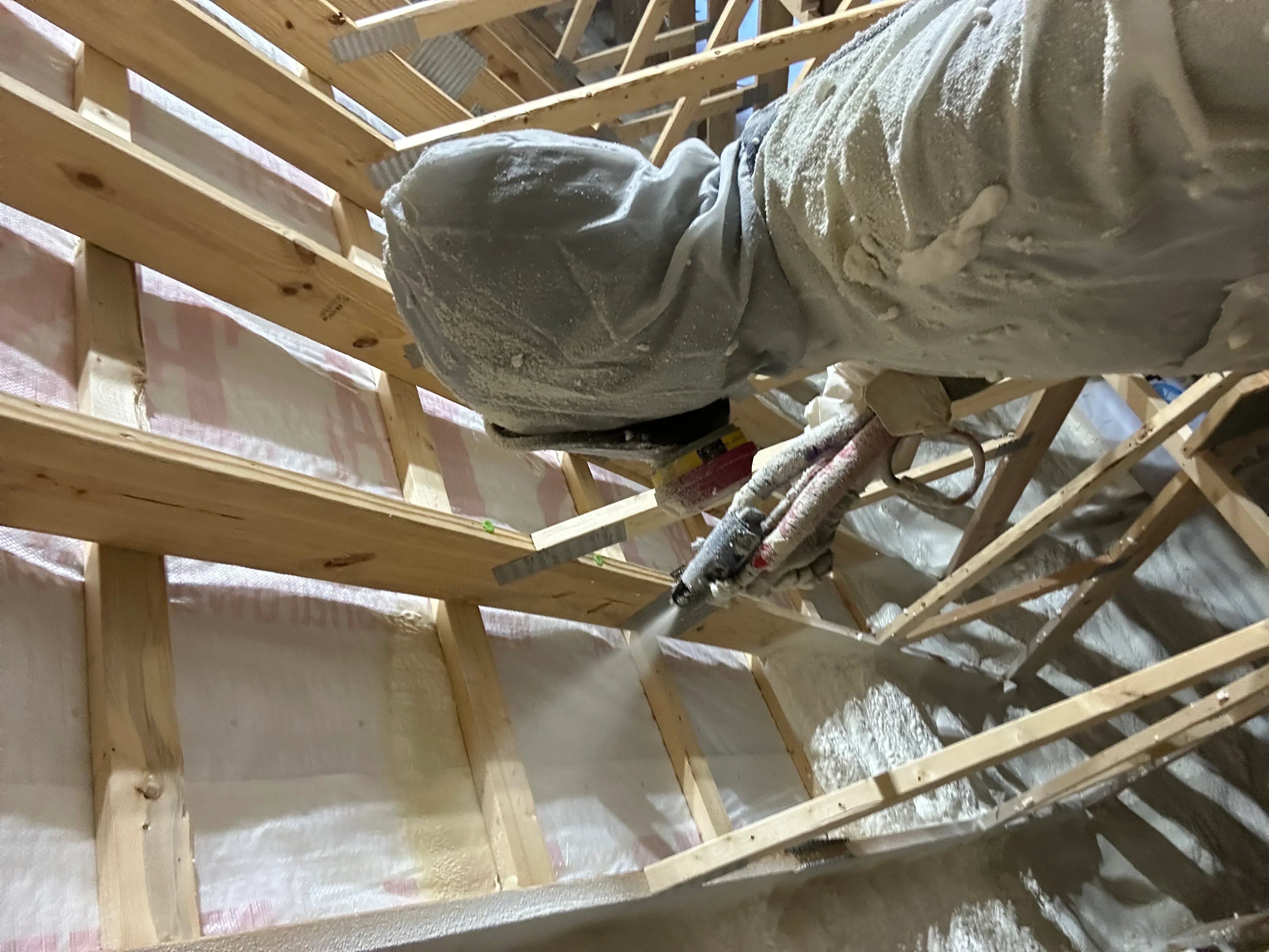 Spray foam insulation being applied to attic rafters and joists with professional equipment
